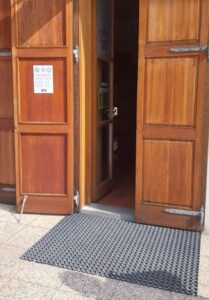 Lesena vrata z oznako "odprto", ki zahtevajo pomoč osebja za dostop zaradi visokega praga in ozkega prehoda.