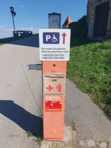 Parkirni avtomat z oznako, ki podrobno opisuje dostop do parkirnih mest za invalide in kontaktne številke za pomoč.